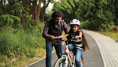Closeup.-Portrait-of-a-little-girl-and-her-father.-Dad-teaching-his-daughter-to-ride-a-bike.-He-lets-her-go.-Moving-camera.-Blurred-background